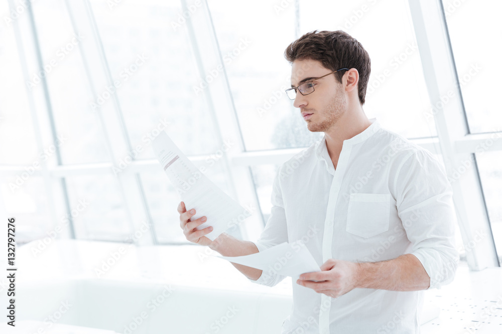 Concentrated man holding documents near big white window.