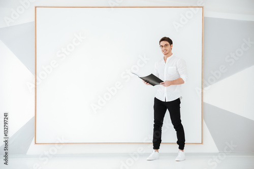 Handsome man holding folder while standing near big board © Drobot Dean