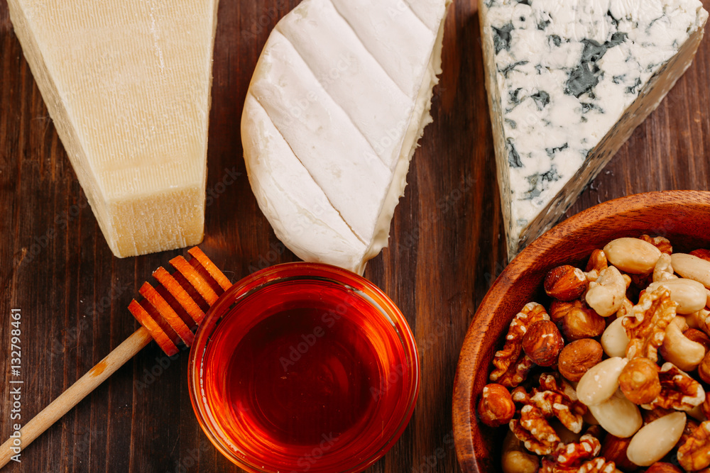 Fototapeta premium Delicious variety of cheese and nuts with honey on old dark wooden table Top view 
