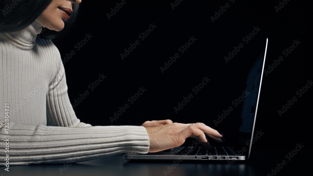 Naklejka premium Young brunette woman typing on her laptop against dark background