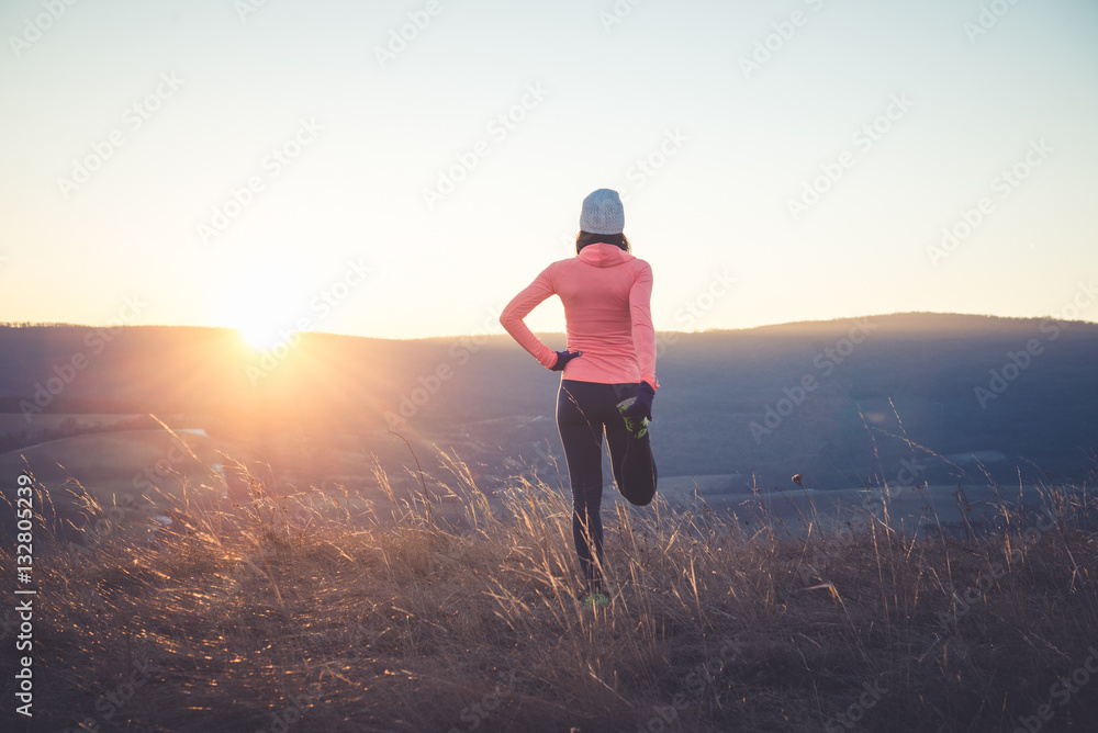 Runner girl stretching on top of the hill