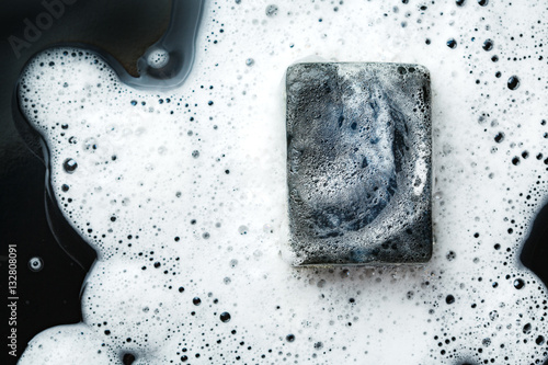 Black coal bar of soap in foam on dark © dariazu