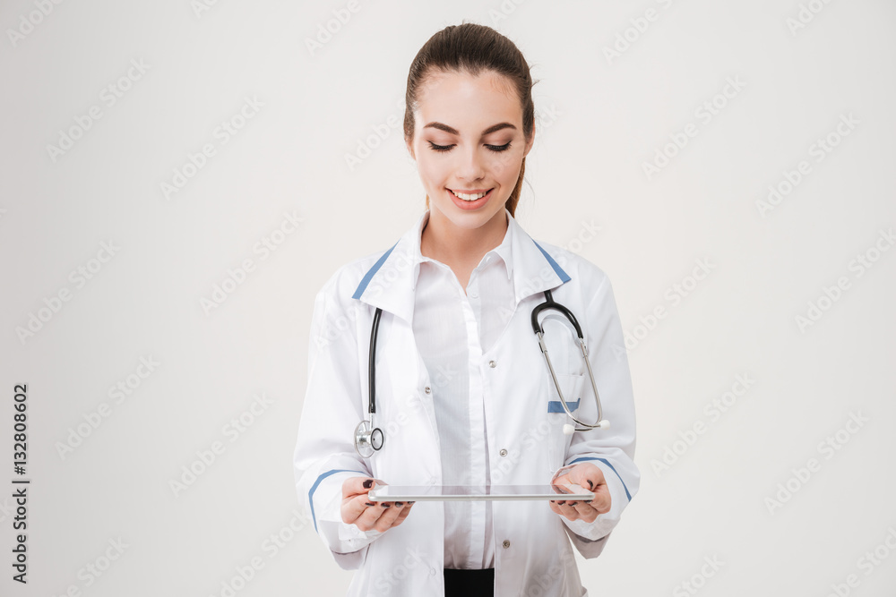 Happy pretty young woman doctor standing and using tablet Happy pretty young woman doctor standing and using tablet