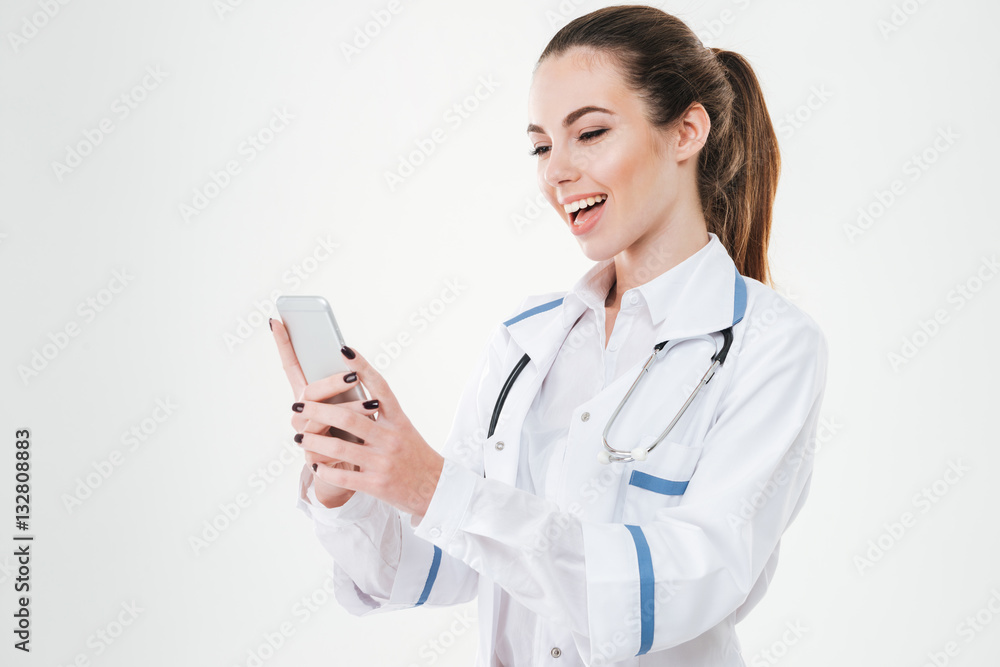 Cheerful young woman doctor standing and using smartphone Cheerful young woman doctor standing and using smartphone