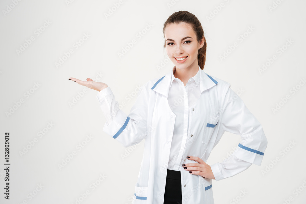 Cheerful pretty young woman doctor holding copyspace on palm Cheerful pretty young woman doctor holding copyspace on palm
