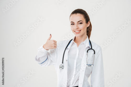 Smiling successful young woman doctor with stethoscope showing thumbs up
