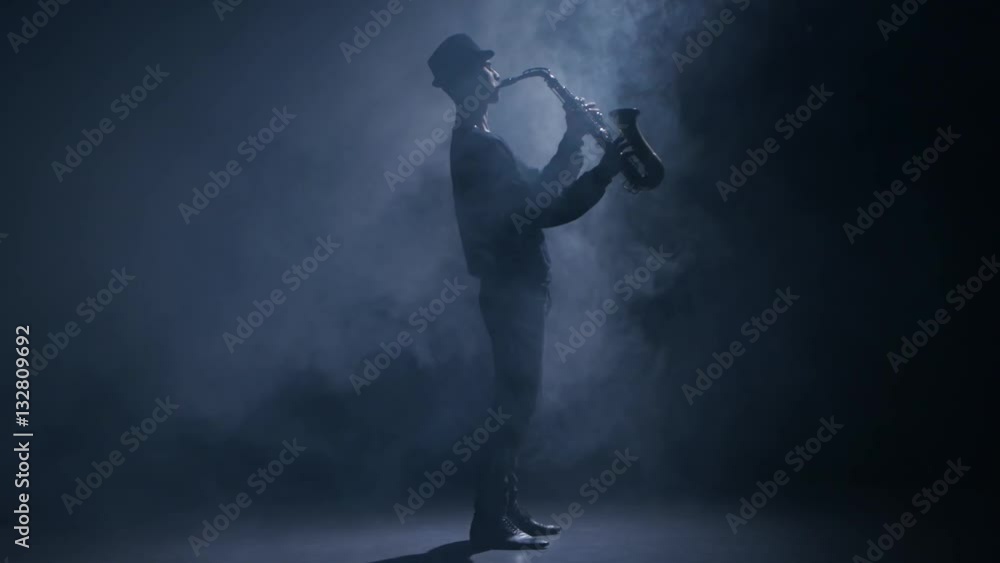 Saxophonist playing a musical instrument in a dark smoky studio Saxophonist playing a musical instrument in a dark smoky studio