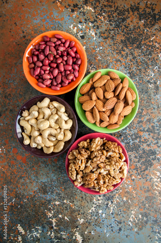 Set of variety of nuts. Almond, peanuts, walnuts and cashew in color ceramic bowls on a rusty background Set of variety of nuts. Almond, peanuts, walnuts and cashew in color ceramic bowls on a rusty background