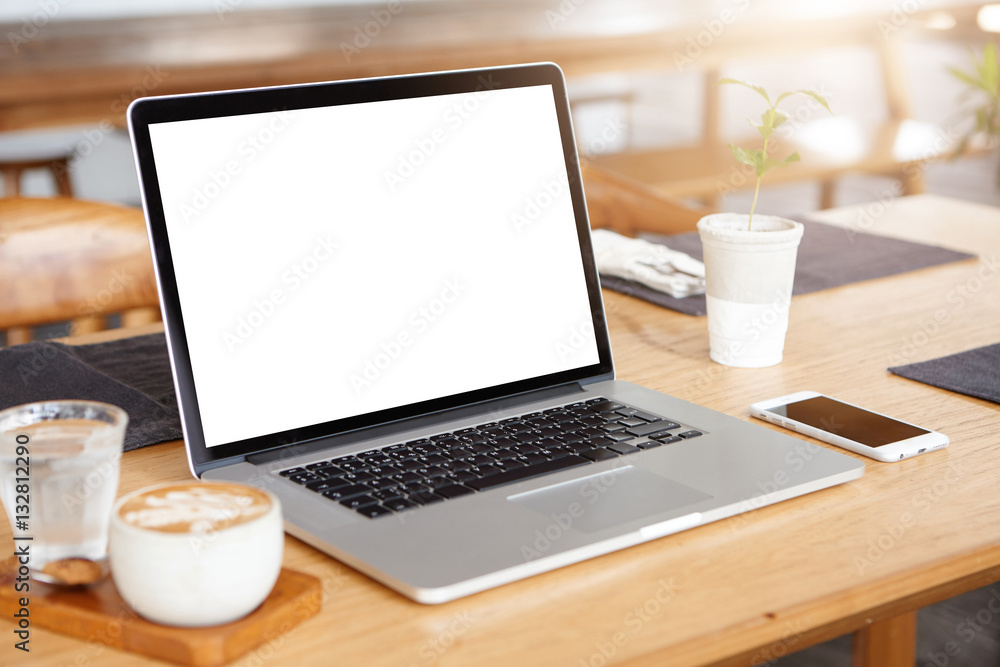 Mockup of generic laptop computer with blank copy space screen for your text or advertising content. Workspace of young freelancer: open notebook pc, cell phone and cappuccino on wooden table Mockup of generic laptop computer with blank copy space screen for your text or advertising content. Workspace of young freelancer: open notebook pc, cell phone and cappuccino on wooden table