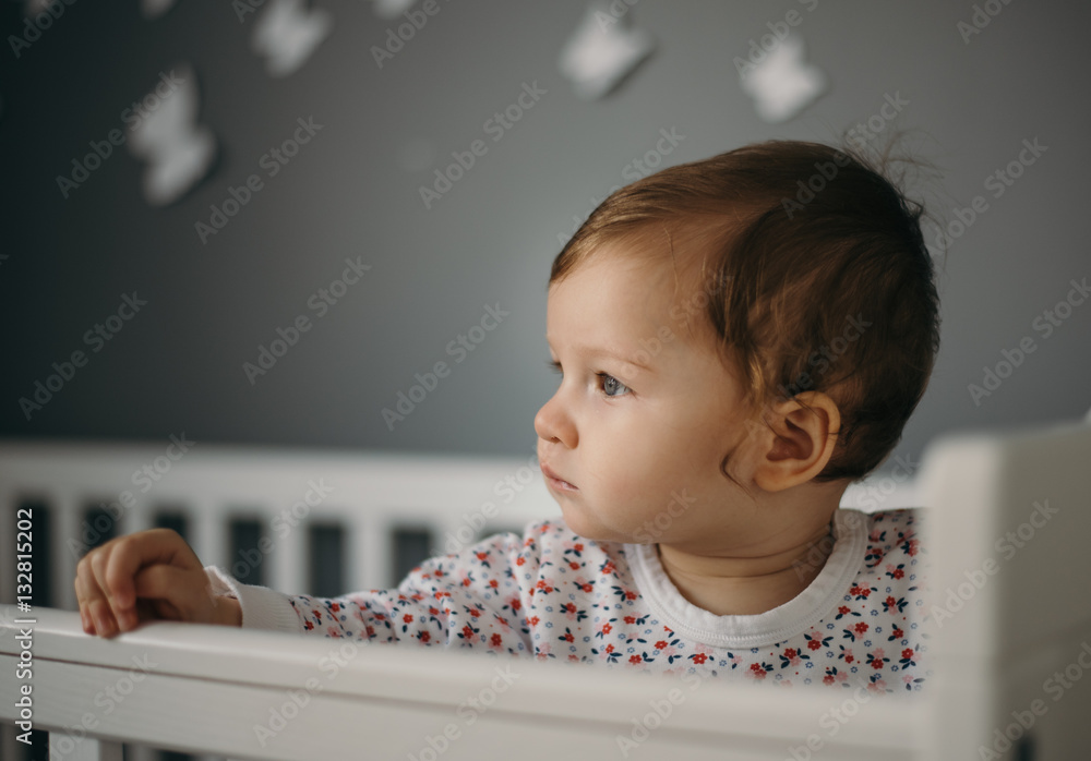 Beautiful, sad little girl indoors portrait in children's room with gray wall and copy space. Baby is nine month old, caucasian. Closeup shot with shallow depth of field. Solitude and sadness concept. Beautiful, sad little girl indoors portrait in children's room with gray wall and copy space. Baby is nine month old, caucasian. Closeup shot with shallow depth of field. Solitude and sadness concept.