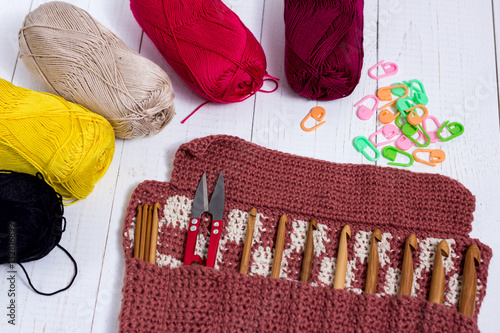 Set of bamboo crochet hooks, color sticker and colorful yarn on white wooden table.