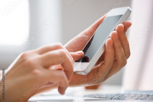 Hands using phone in front of computer, home work place, day time with sun fare