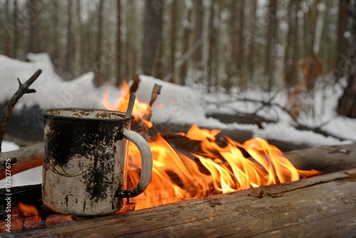 Железная кружка греется на костре на огне зимой в лесу