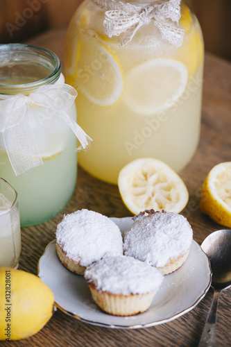 Delicious refreshing ice cold lemonade in glass two jars and some cottage cheese muffins on the wooden table