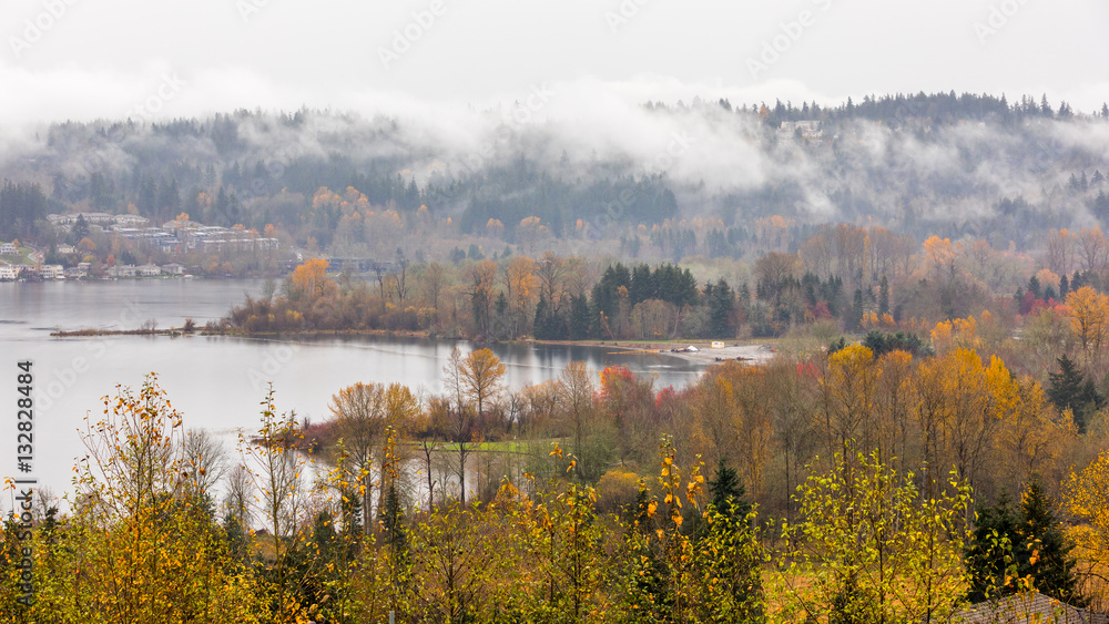 River bank in the mist, autumn forest on the riverside, beautiful trees and small houses on a background of mountains River bank in the mist, autumn forest on the riverside, beautiful trees and small houses on a background of mountains