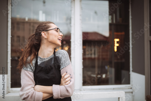 Happy young woman confectioner standing with arms crossed near cafe