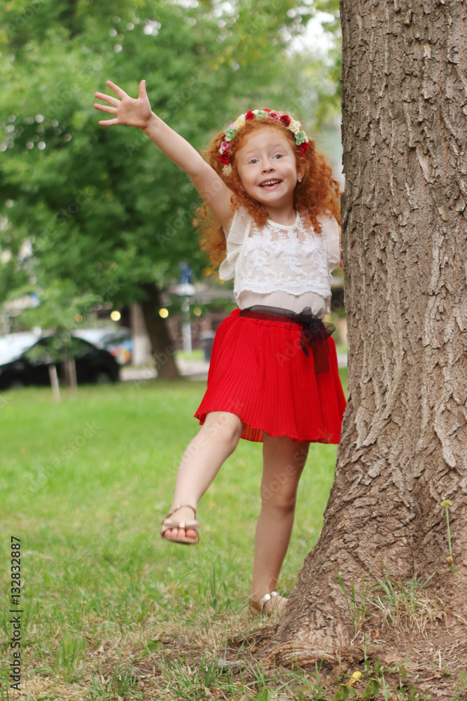 Little happy girl poses near big tree in summer park, shallow do Little happy girl poses near big tree in summer park, shallow do