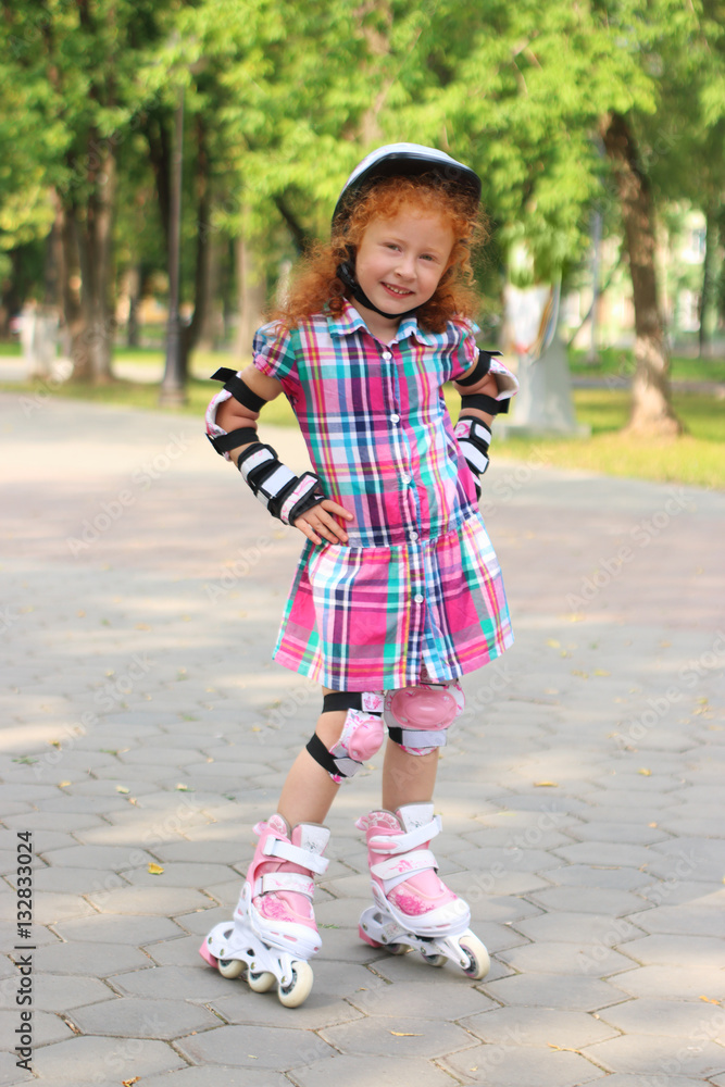 Fototapeta premium Happy little girl in helmet roller skates in summer park, shallo
