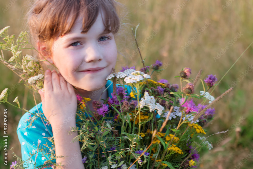 Happy little girl holds wild flowers and smiles in dry field at Happy little girl holds wild flowers and smiles in dry field at