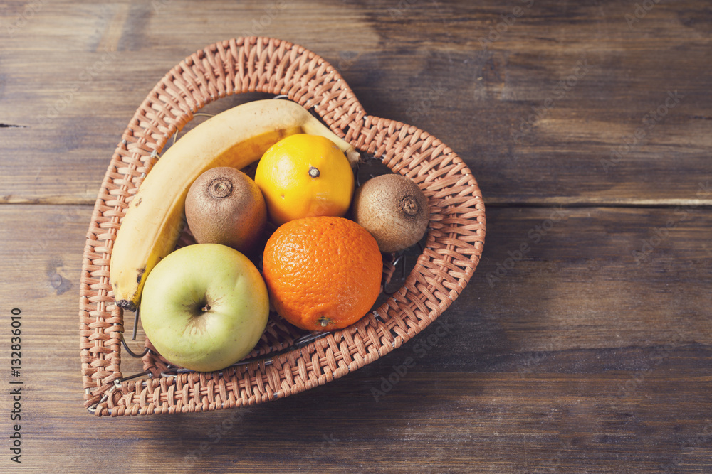 Basket in the background of the heart with fruit, bananas, apples, kiwi, lemon on an old vintage background of wooden boards