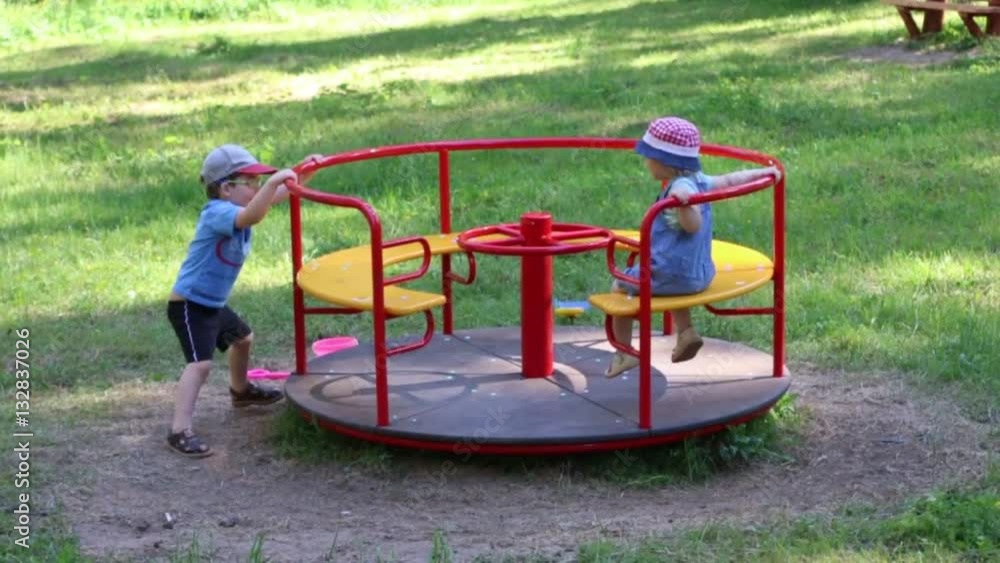 Happy little boy and girl play with carousel in summer green park Happy little boy and girl play with carousel in summer green park