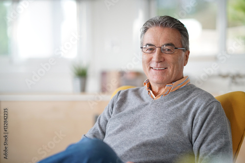 Smiling senior man with eyeglasses relaxing in armchair photo