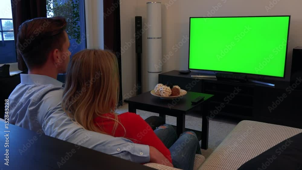 A young couple watches a TV with a green screen in a cozy living room A young couple watches a TV with a green screen in a cozy living room