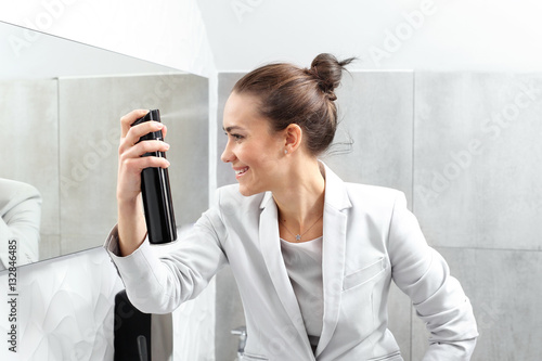 Elegancka pracownica biura.
Kobieta biznesu czesze i lakieruje włosy w firmowej toalecie.
 photo