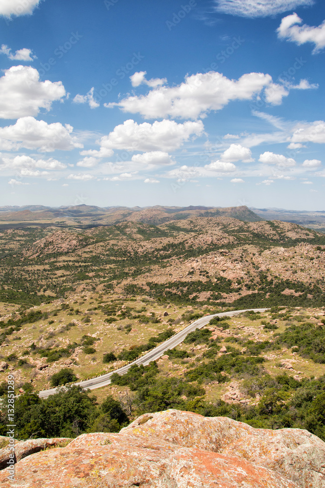 Mountain road winding through an arid landscape between outcrops of rock at Wichita Mountains