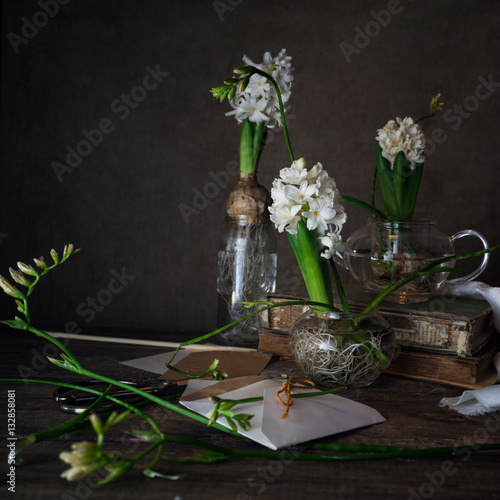 three white hyacinth and freesia in transparent vases, letter, envelope on a dark background