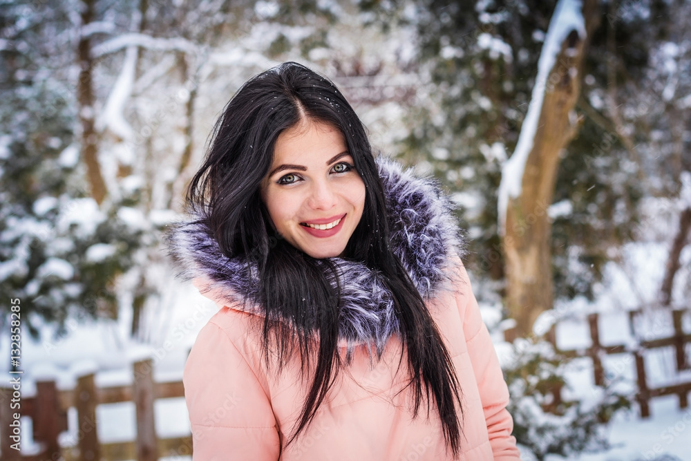 Brunette girl standing on the background of snow and trees and smiling Brunette girl standing on the background of snow and trees and smiling