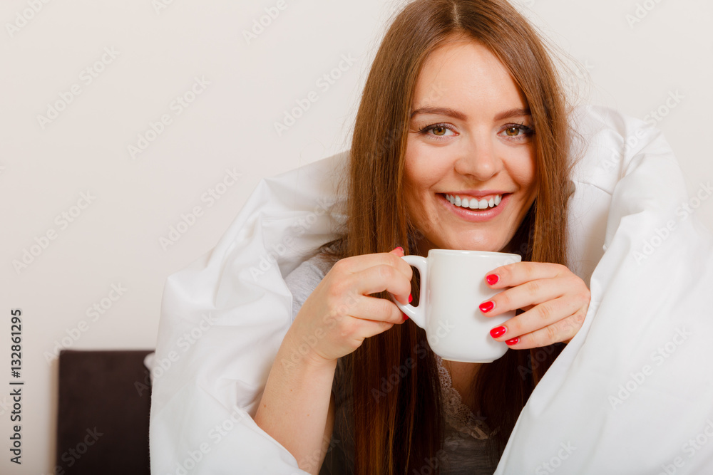 Smiling woman holding cup of drink in bed Smiling woman holding cup of drink in bed
