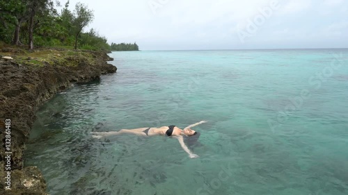 Young slender woman in black swimsuit is lying on the water of caribbean sea photo