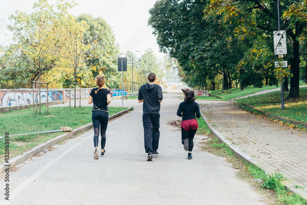 Three women and man runners from back running outdoor in city park in autmun - runners, training, athlete concept Three women and man runners from back running outdoor in city park in autmun - runners, training, athlete concept
