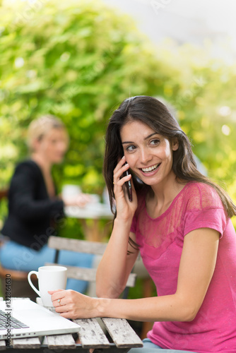 Cheerful woman sitting at a terrace cafe using a smartphone