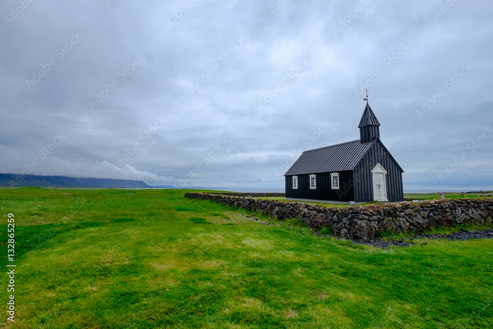 Black Icelandic church in a field of grass under a cloudy sky