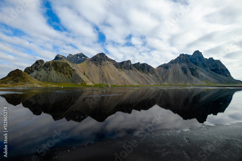 Vestrahorn mountain under a cloudy blue sky with reflection in water