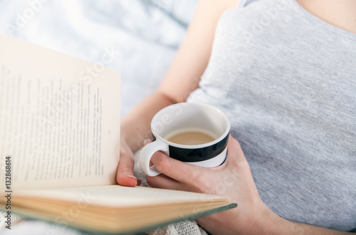 Girl reading book and drinking coffee in bed at home