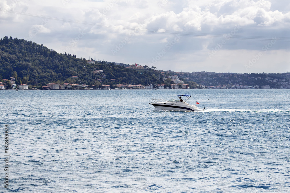 Obraz premium Luxury yacht / boat crosses Bosphorus between European and Asian sides in Istanbul. It is cloudy autumn day. It is internationally-significant waterway located in northwestern Turkey