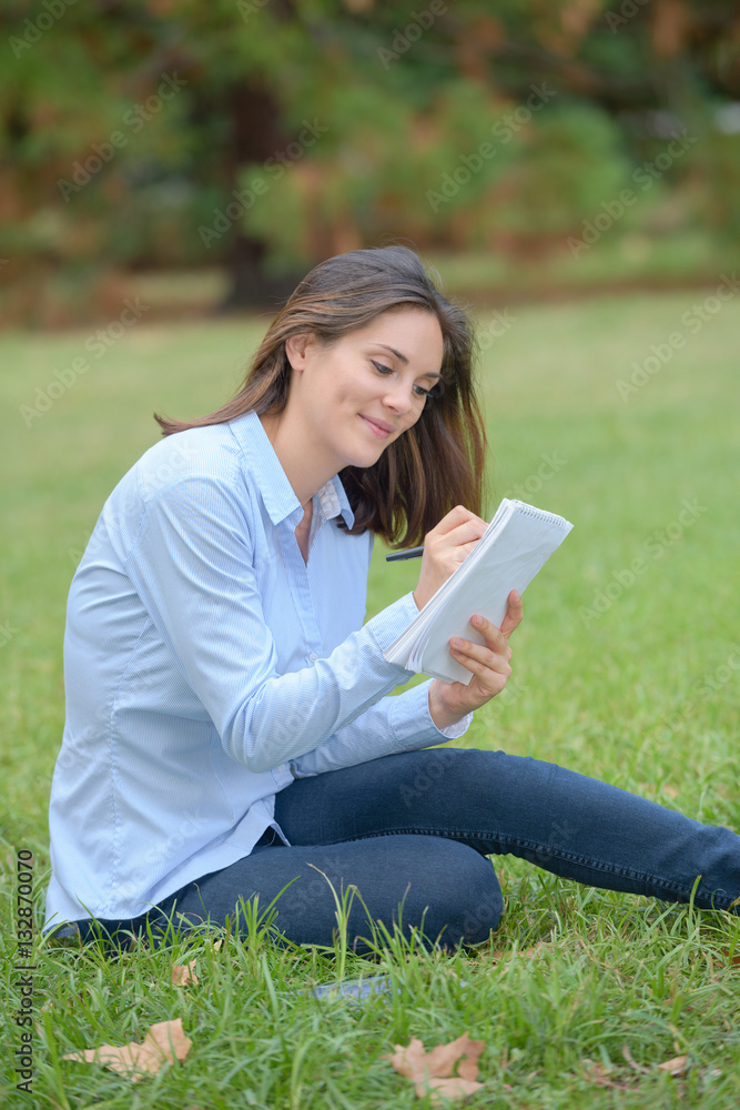 Obraz premium Woman sat in park writing in notepad