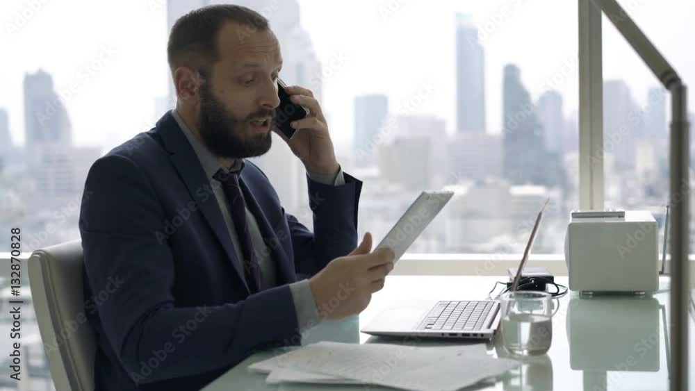 Angry businessman with tablet and laptop talking on cellphone in office
Angry businessman with tablet and laptop talking on cellphone in office