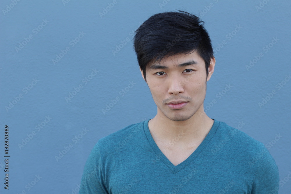 Asian man with serious expression over blue background with copy space Asian man with serious expression over blue background with copy space