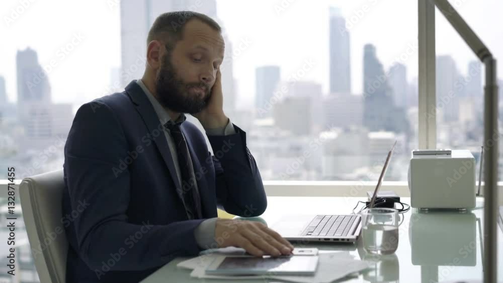 Young, bored businessman sitting by desk in office
Young, bored businessman sitting by desk in office