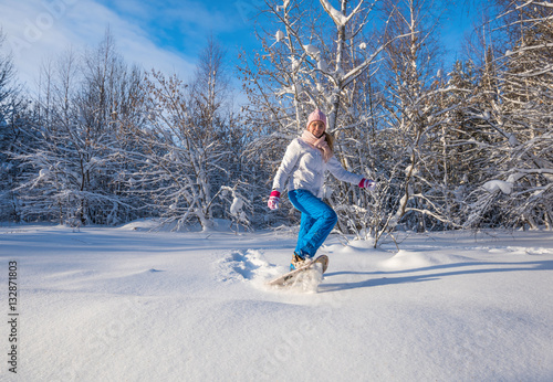 Winter sport activity. Woman with snowshoes on fluffy snow in forest. Beautiful landscape with coniferous trees and white snow.