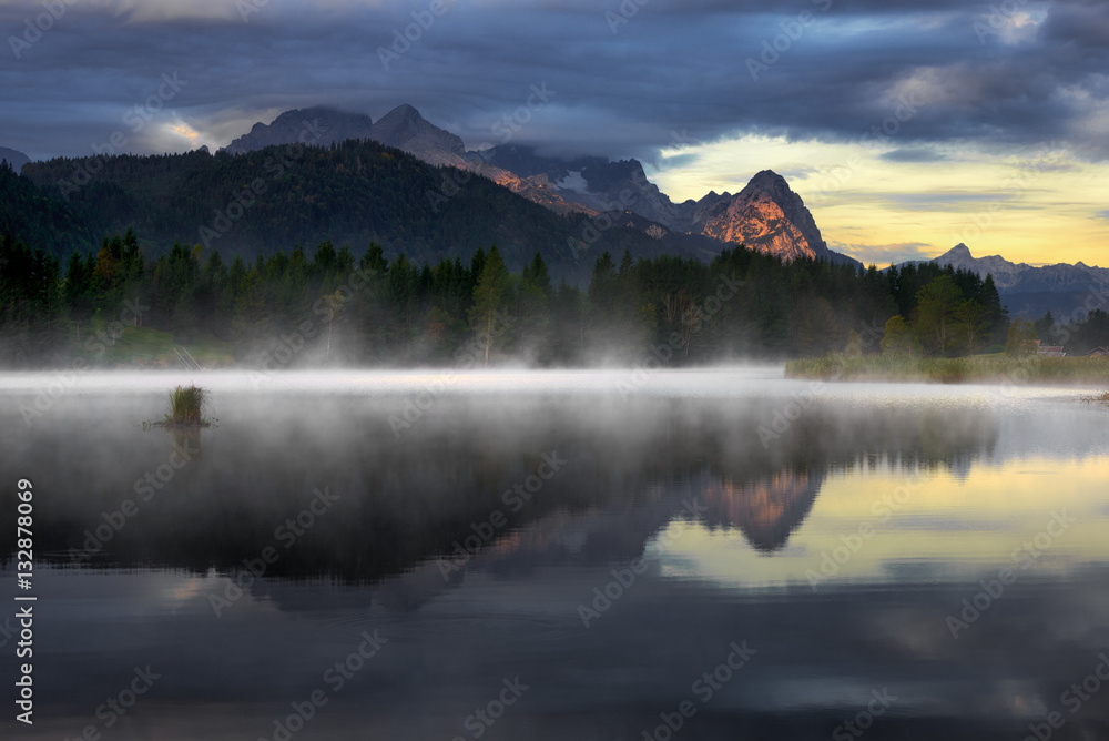Wetterstein mountain reflection during autumn day with morning fog over Geroldsee lake, Bavarian Alps, Bavaria, Germany.