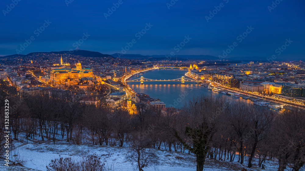 Budapest, Hungary - Panoramic skyline view of the Buda Castle (Royal Palace), Chain Bridge, Danube River and the Parliament at blue hour as seen from Gellert Hill in winter time