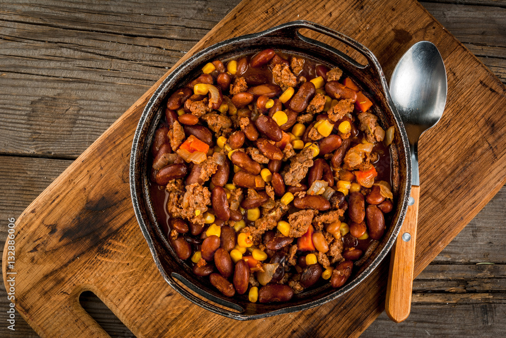 Traditional Mexican and Chilean dish of chilli con carne. In the rustic pan, next to tortillas and fresh vegetables on a wooden table, copy space Traditional Mexican and Chilean dish of chilli con carne. In the rustic pan, next to tortillas and fresh vegetables on a wooden table, copy space