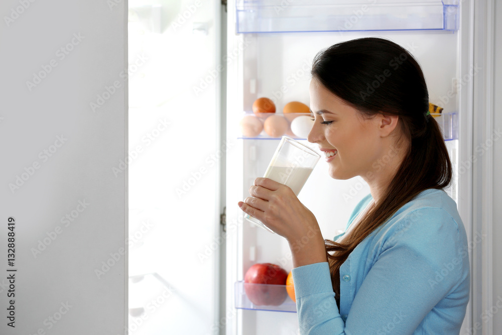 Young woman drinking milk beside open fridge Young woman drinking milk beside open fridge