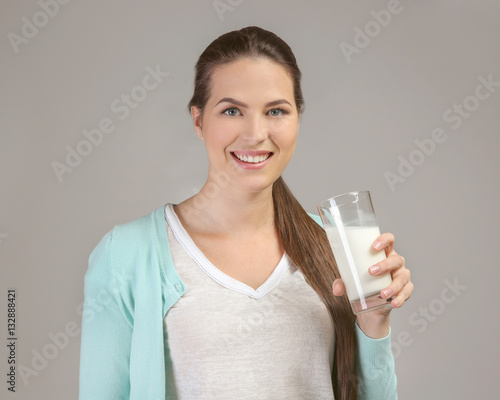 Young attractive woman with glass of milk on grey background