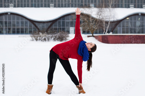 Young brunette woman doing fitness workout outdoors against snowy field and a building with large windows
